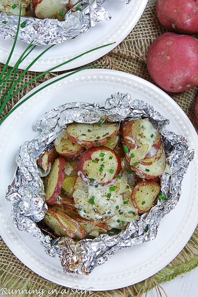 Two white plates with the grilled potatoes in foil.