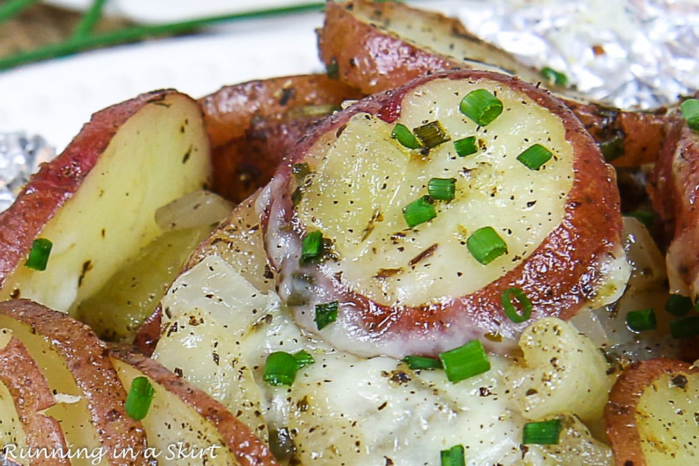 Close up of grilled potatoes in foil with chives on top.