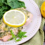 Salmon with a lemon slice and salad on a white plate.