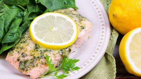Salmon with a lemon slice and salad on a white plate.