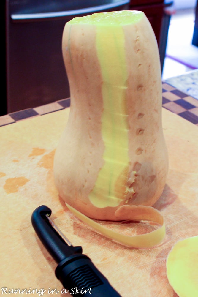 Whole butternut squash on a cutting board with vegetable peeler showing how to cut the squash.