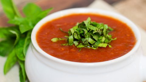 Easy Crock Pot Tomato Basil Soup in a white bowl with basil garnish on top.