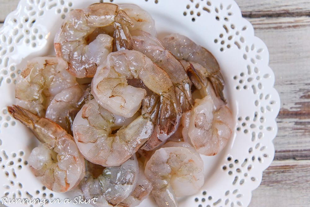 Raw shrimp for the recipe on a white plate.