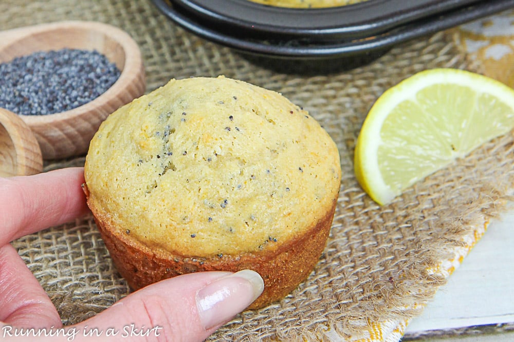 Hand holding a Healthy Lemon Poppy Seed Muffin with a lemon slice and poppy seeds.