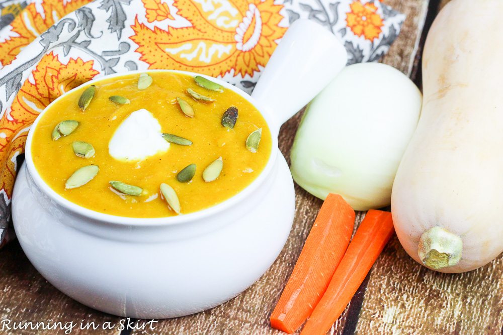 Bowl of butternut squash soup next to butternut squash and carrots.