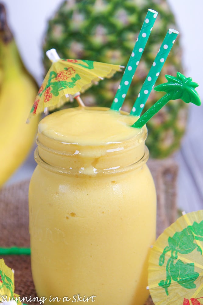 Mango smoothie in a glass jar with pineapple in the background.