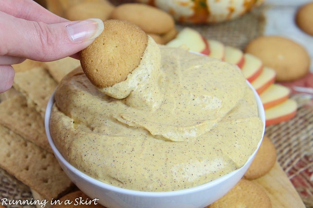 Close up of hand holding vanilla wafer and dunking into the Healthy Cheesecake Pumpkin Dip.