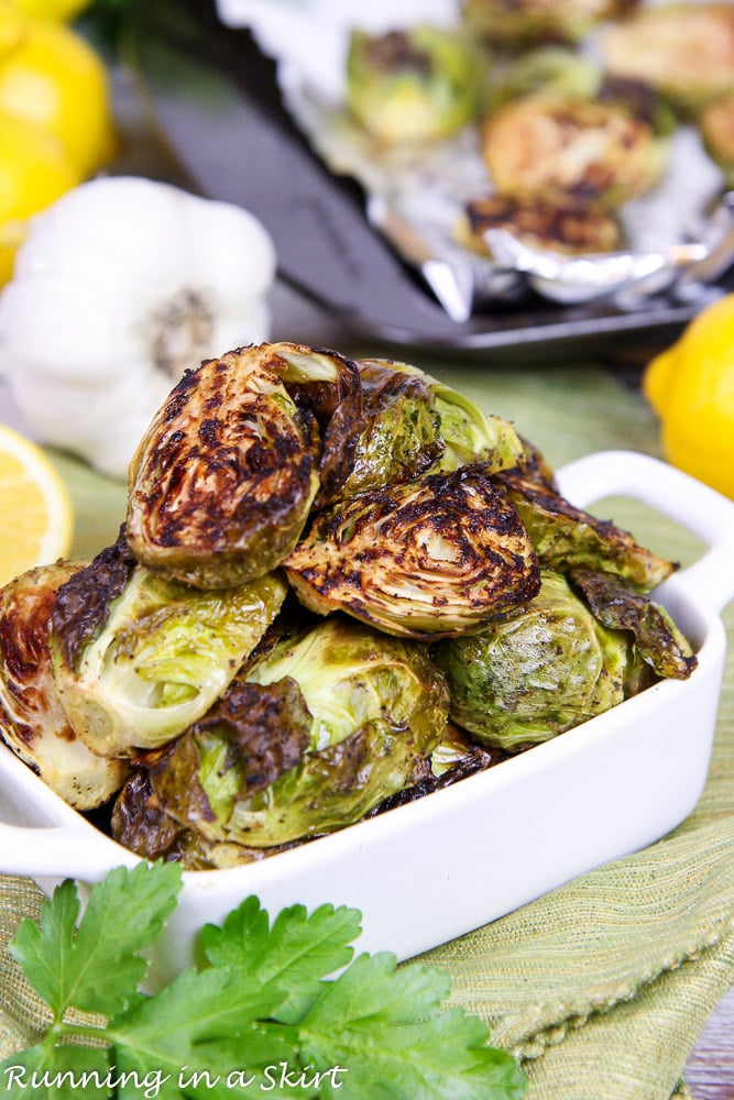 Roasted Brussels Sprouts with Garlic and Lemon in a white dish showing baking sheet in the background.