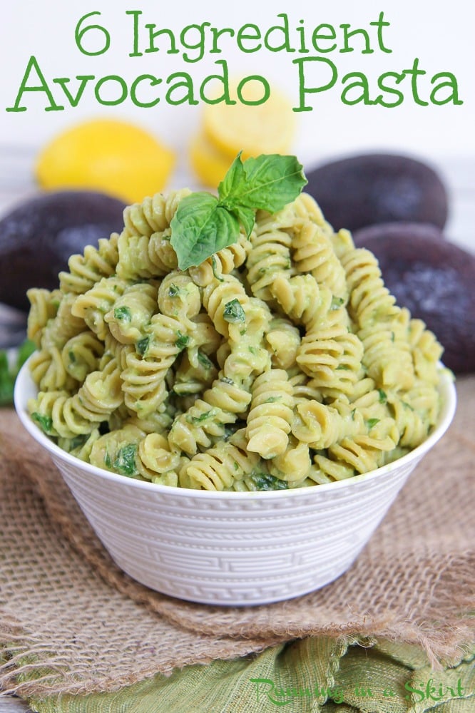 Bowl of creamy avocado pasta with avocado and lemon in the background.