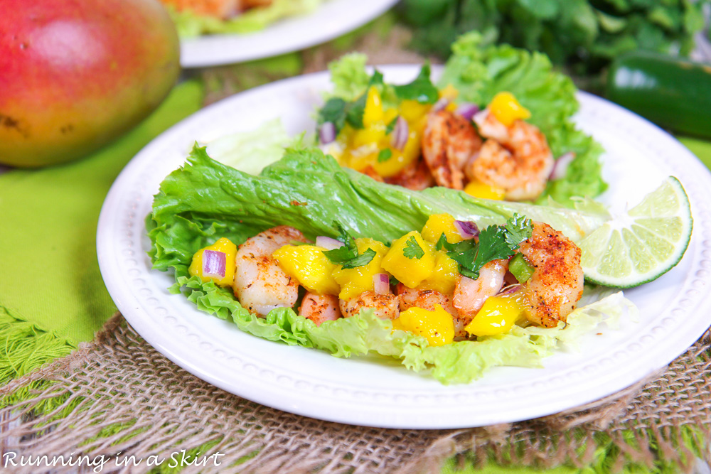 Lettuce Wrap Shrimp Tacos on white plate with lime and mango in the background.