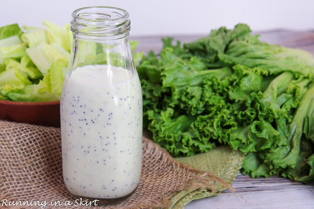 Glass bottle with creamy Greek Yogurt Poppyseed Dressing in front of salad greens.