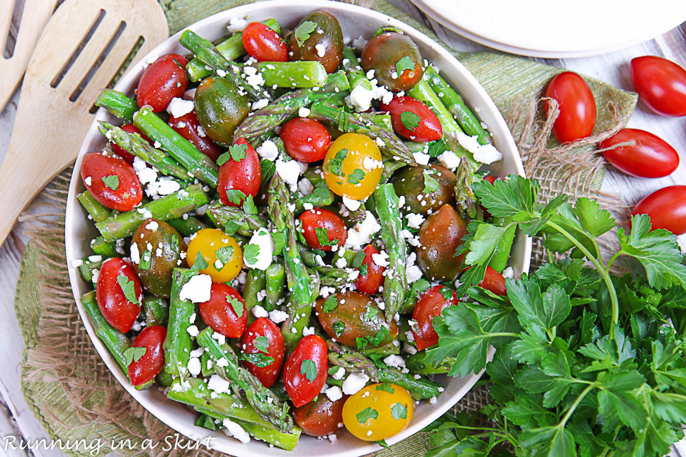 Overhead shot of the Asparagus and Tomato Salad in a bowl with fresh herbs on the side.