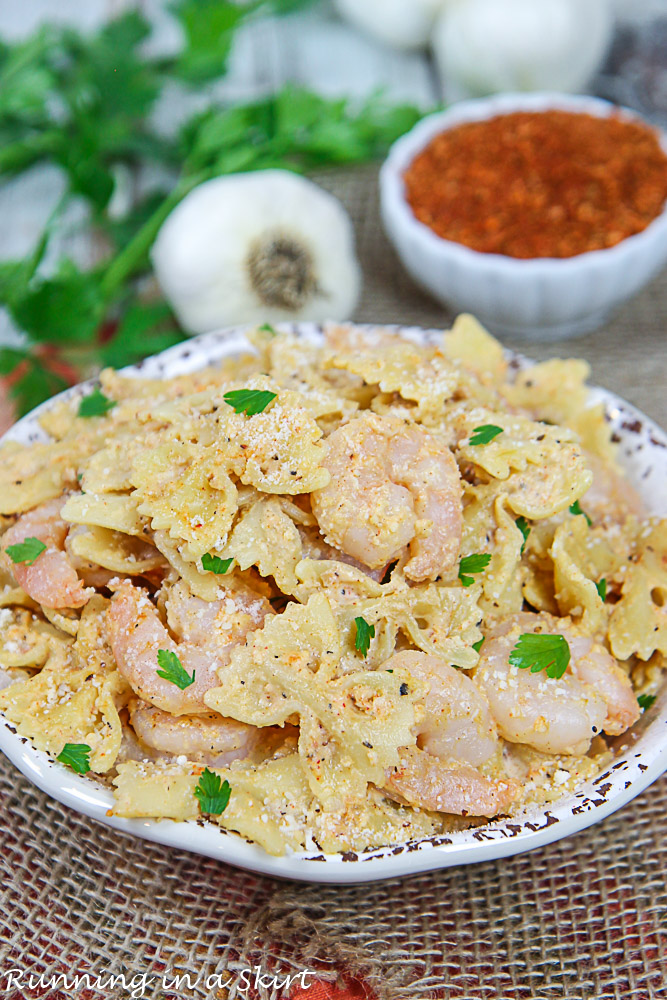 Cajun Shrimp Pasta Recipe in a bowl with Cajun Seasoning, garlic and parsley in the background.