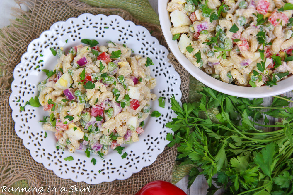 Overhead shot of Healthy Macaroni Salad on a white plate and a serving bowl on the side.