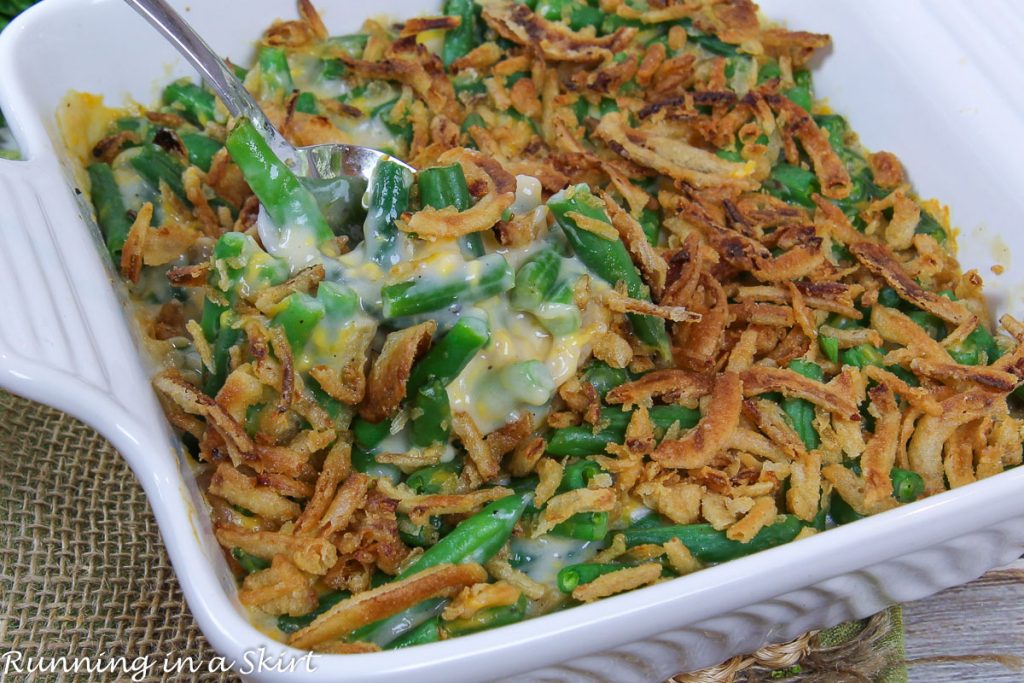 Cheesy Green Bean Casserole with fresh green beans in a casserole dish with a spoon.
